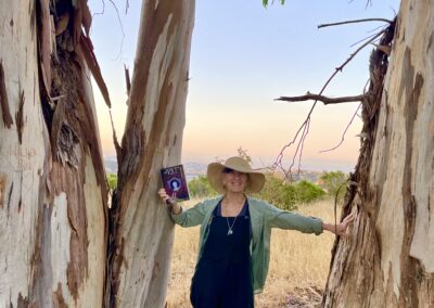 YA Author Annie Fox holds up “The Little Things That Kill: A Teen Friendship Afterlife Apology Tour” in the eucalyptus grove featured in her novel. Fans of the books We Were Liars and A Good Girl's Guide to Murder will love this young adult paranormal mystery.